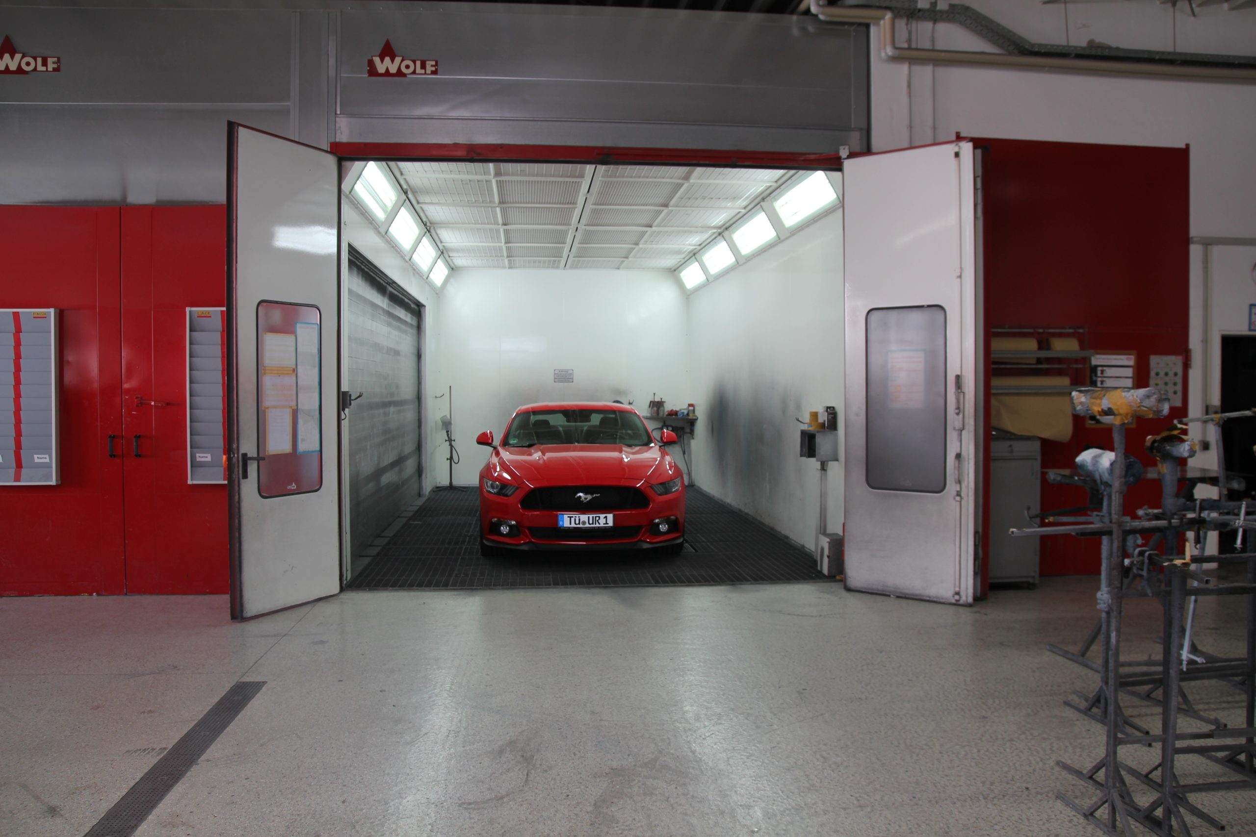 Rote Lackierkabine mit geöffneten Türen, darin ein roter Ford Mustang in der Vorbereitung zur Lackierung